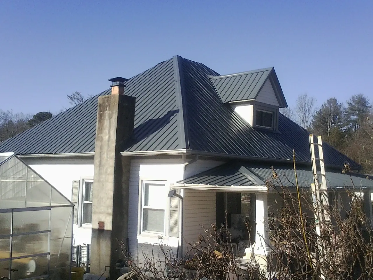 Dark blue standing seam metal roof on a white farmhouse with dormer — Slate & Tile Roof Repair by Roofing Brothers in Goddard