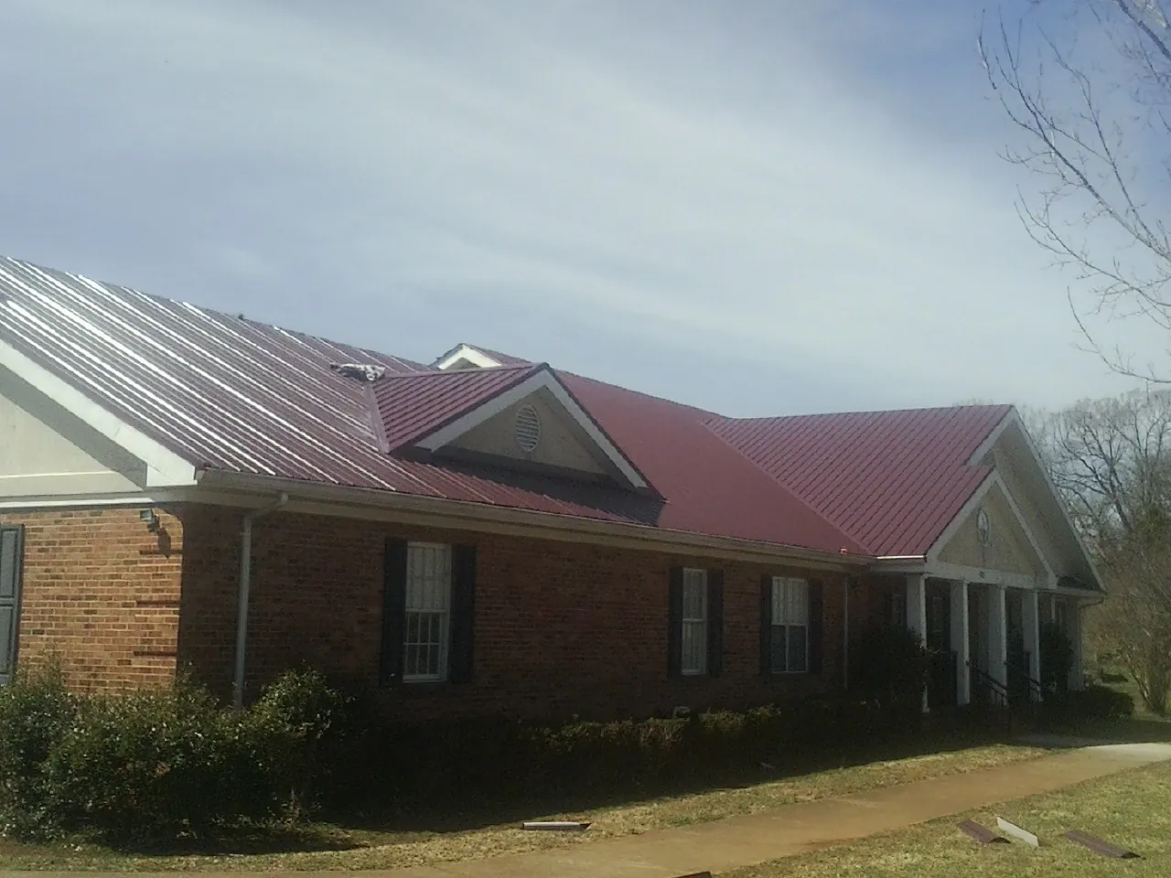 Red metal roof with gabled entries on a long brick building, from a Hail Damage Roof Repair job in Goddard