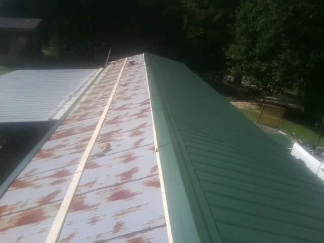 Old rusted panels beside newly installed green metal roofing — Wind Damage Roof Repair by Roofing Brothers in Goddard