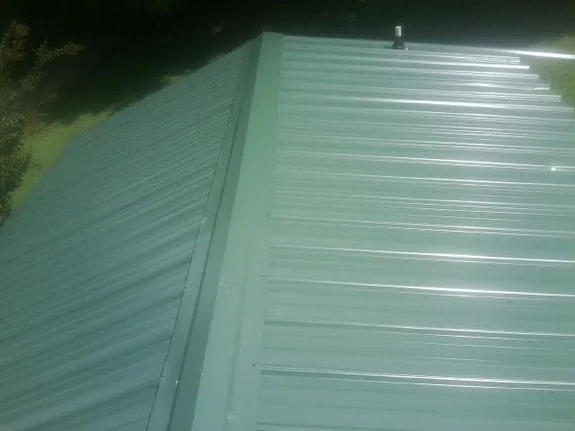 New green metal panels meeting at the ridge of a roof — Flat Roof Repair work by our crew in Goddard