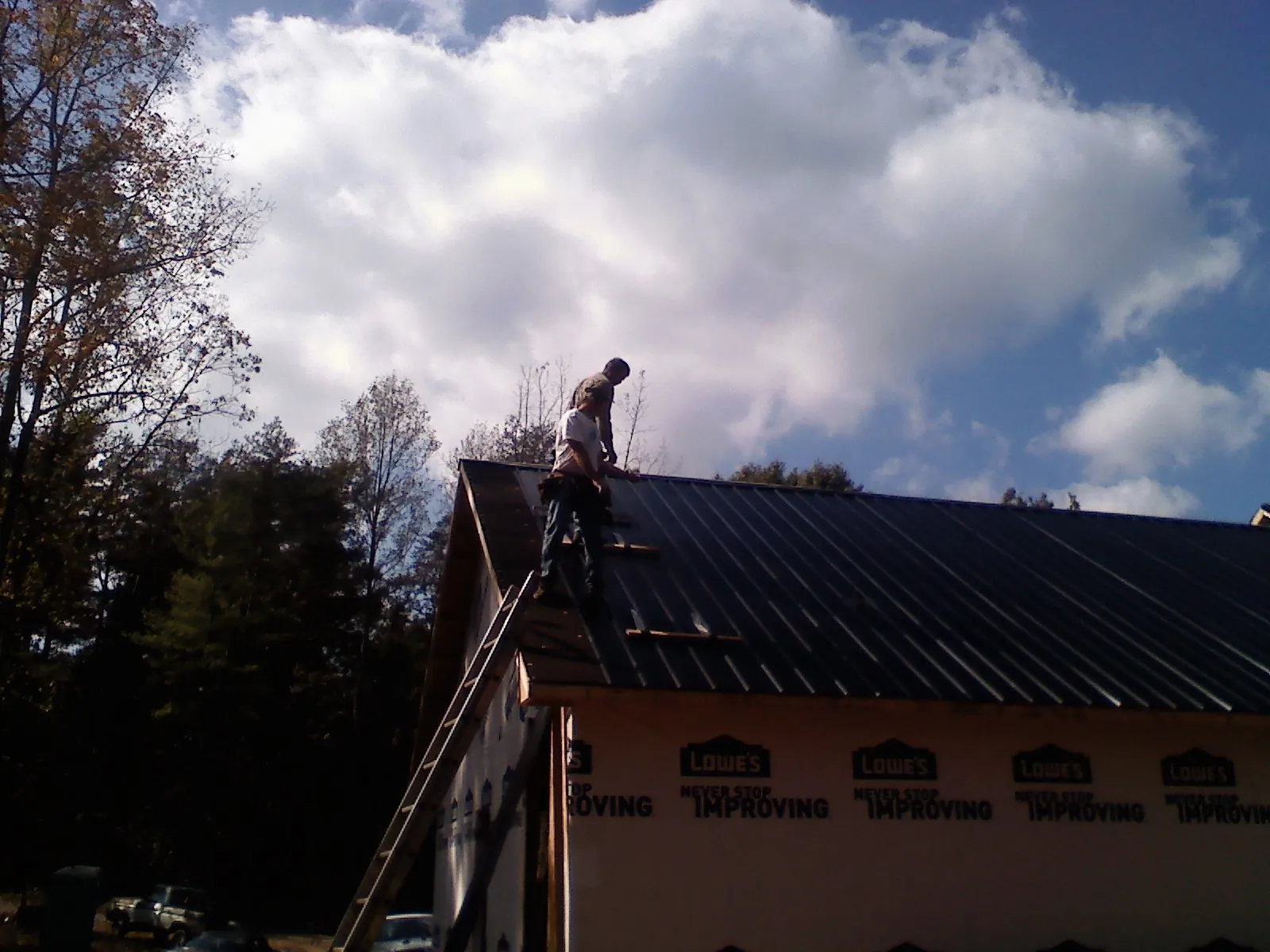 Roofer fastening dark metal panels high against a cloudy sky, from a Roof Inspection job in Goddard