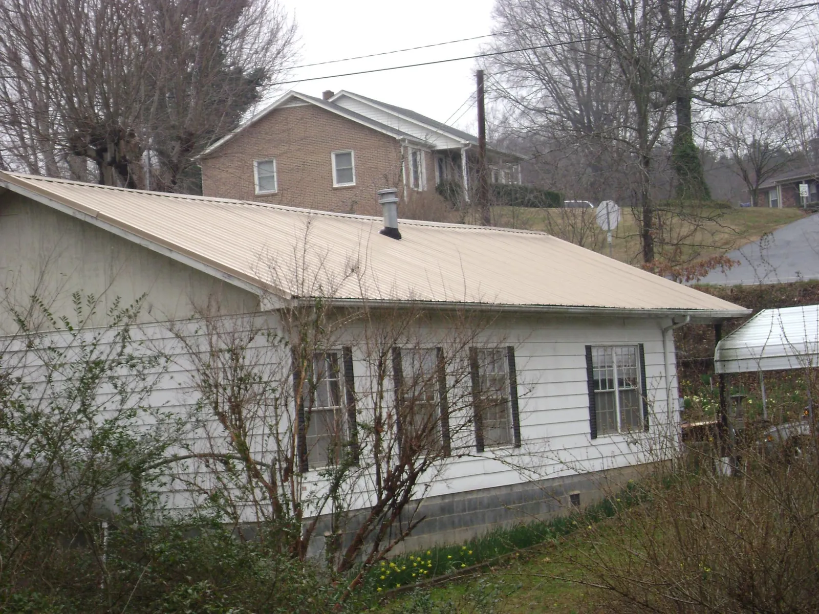 Tan metal roof on a white sided house set into a hillside — Commercial Roofing by Roofing Brothers in Goddard