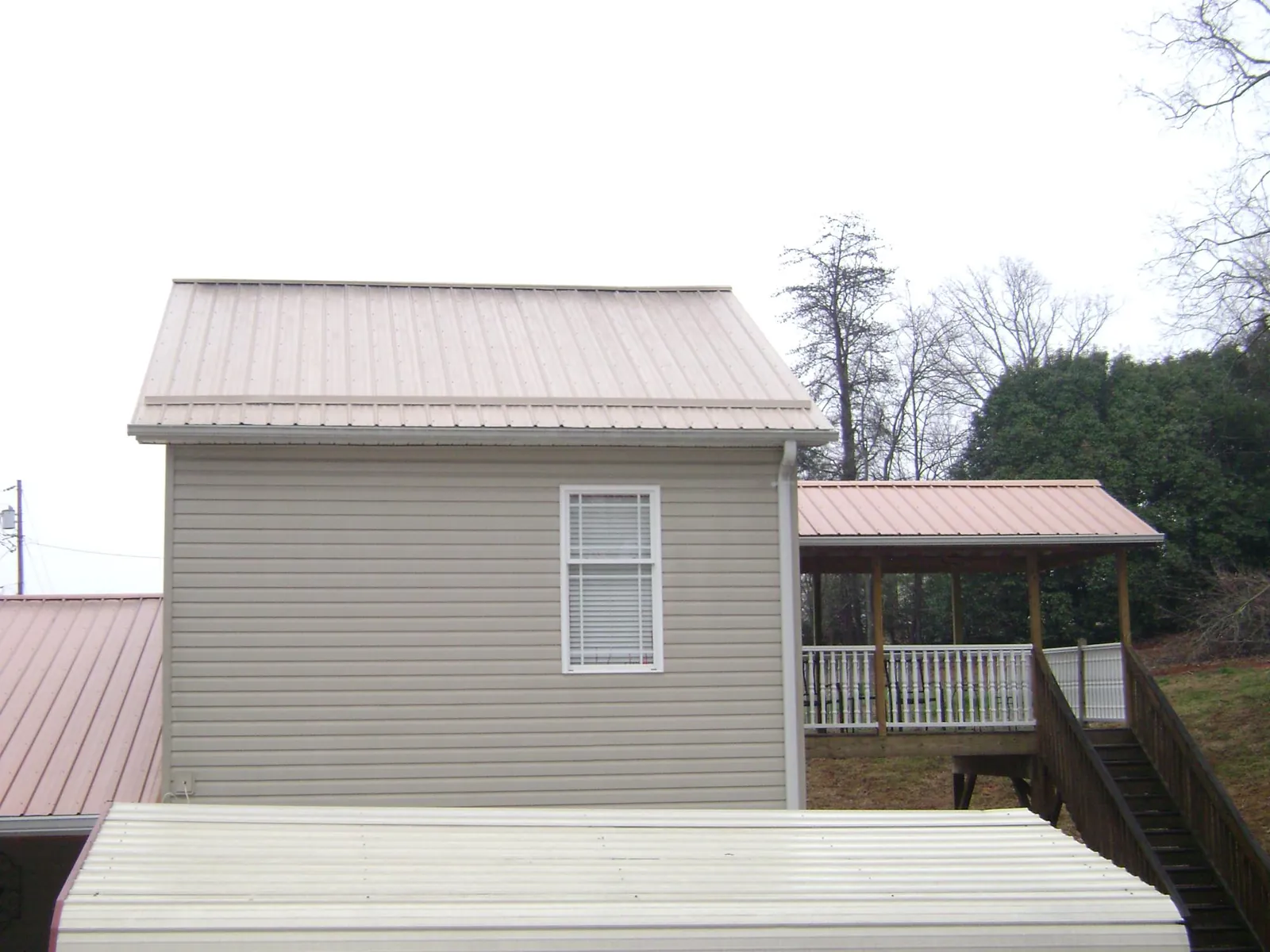 Tan metal roofs on a two story addition and attached porch, from a Roof Replacement job in Goddard